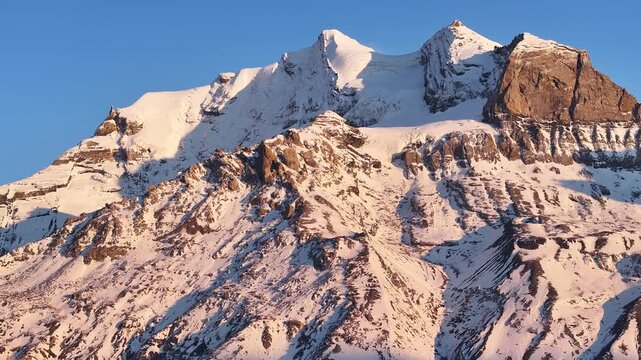 Aerial view of majestic snow-covered mountains under a clear blue sky, contrasting textures, and tones, Kandersteg, Canton of Bern, Switzerland.