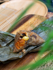 Traditional Thai sticky rice dumpling zongzi wrapped in dried leaves with savory filling on rustic wooden plate