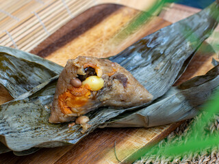 Traditional Thai sticky rice dumpling zongzi wrapped in dried leaves with savory filling on rustic wooden plate