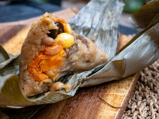 Traditional Thai sticky rice dumpling zongzi wrapped in dried leaves with savory filling on rustic wooden plate