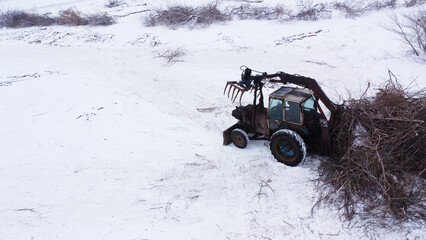 Industrial tractor with hydraulic grapple clearing brush in winter field © Andrey