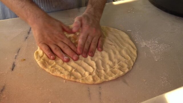 A chef kneads pizza dough, flattens it into a round shape, flips it, and coats it in flour. Perfect for content about cooking and food preparation.