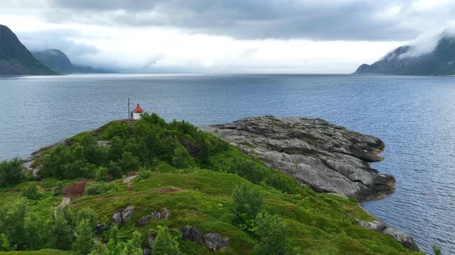 Aerial, forward turn, drone flight, above husoy island. Small island, small lighthouse, greenery and rocks. View towards open ocean, mountains on both sides. Amazing wild nature in summer on Senja isl