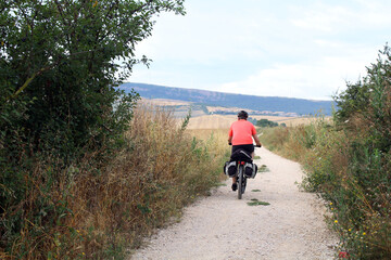 Obraz premium People cycling on a dirt path along the Camino de Santiago with farms and open rural scenery in Navarra Spain 2024
