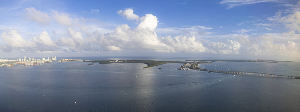 Aerial view of a bridge stretching across the water towards the distant skyline, contrasting with the vast blue sea and fluffy white clouds, Key Biscayne, Florida, United States.