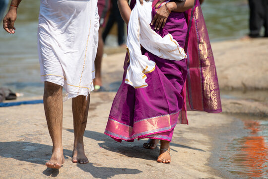 Indian couple walking beside river, dressed in colorful traditional clothes, woman wearing purple sari, man with white lungi, culture, religion and tradition, India