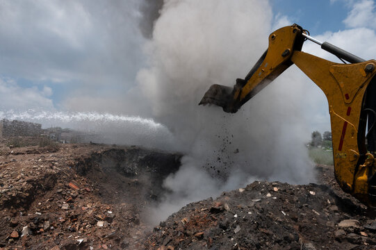 A cloud of smoke and steam explodes as excavator assisting firefighters to extinguish an underground fire on an illegal waste dump in Kyasands, South Africa.