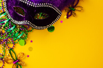 Mardi Gras background with carnival mask, beads, fleur de lis on yellow table. © photoguns