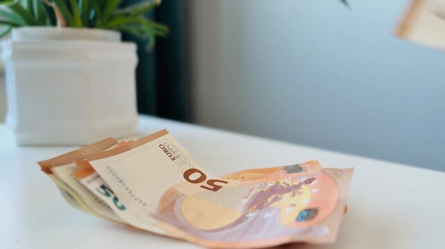 A woman places 50 euro banknotes into a neat stack on a white table. The video illustrates cash handling, savings, income, and personal finance concepts in a clean, minimal setting. Suitable for theme