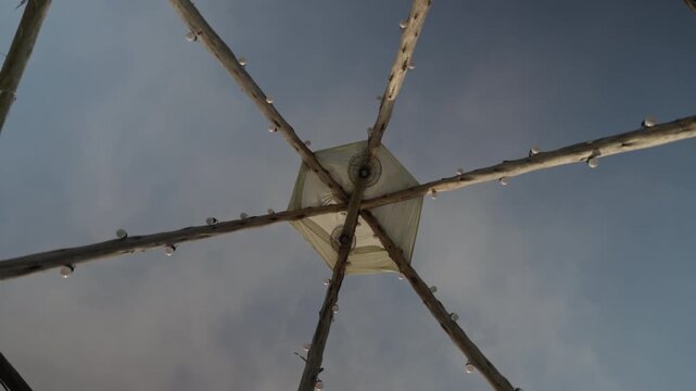 Low angle view of a wooden tipi structure with fairy lights against a clear blue sky in daytime.