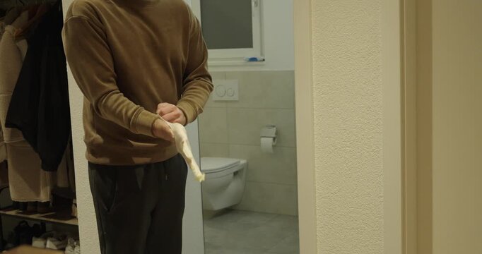 Man in a bathroom preparing protective gloves and a face mask as a precaution against norovirus infection. Concept of hygiene measures, infection prevention, home healthcare, and personal safety.