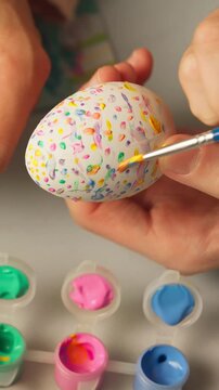 Close view of brush applying soft pastel dots on egg during easter tradition decoration, vertical
