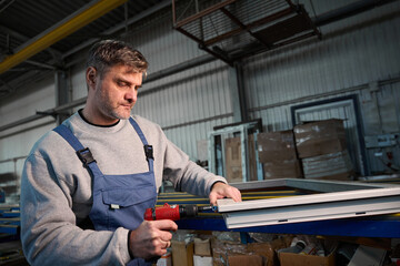 Repairman in workshop using drill to work on production of PVC windows
