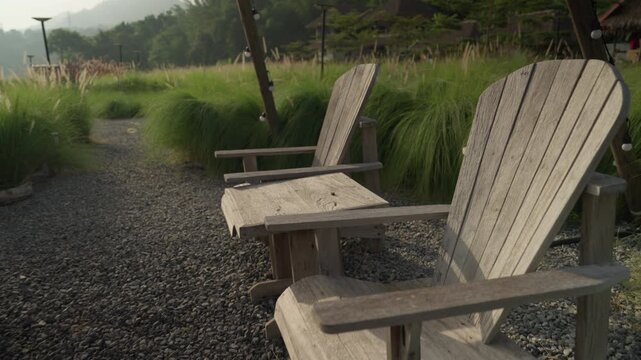 Morning atmosphere of a cozy glamping spot with a wooden tipi structure, table, and chairs in a lush green meadow with white wildflowers.