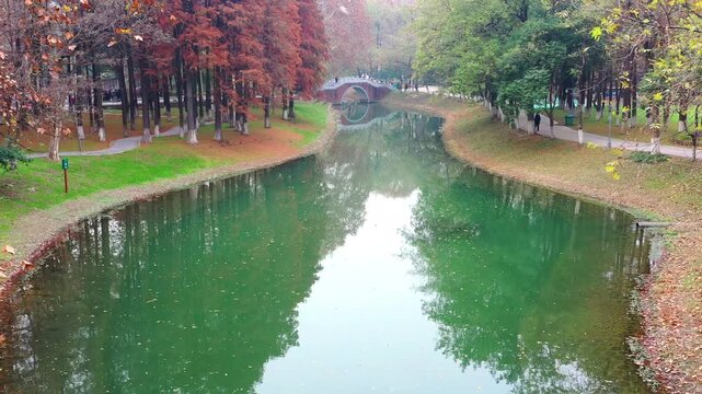 Autumn Canal Park with Bridge and Falling Leaves