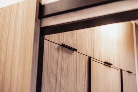 A close-up view of sleek vertical wood cabinets featuring modern black handles and clean linear design under a black frame