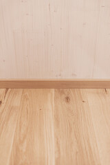 A symmetrical view of natural wooden floorboards meeting a light wood wall with oak skirting, featuring clean lines and copy space