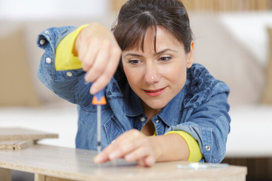 woman assembling wooden furniture using screwdriver