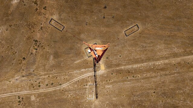 Aerial view of an orange triangular structure casting a stark shadow on the arid landscape, a geometric anomaly in the vast expanse, Cape Town, Western Cape, South Africa.