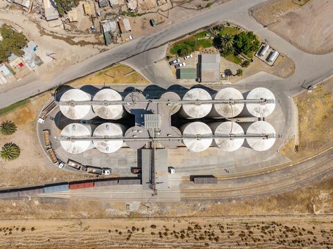 Aerial view of a grain silo complex casting long shadows across the arid landscape, juxtaposed against the nearby settlement, Cape Town, Western Cape, South Africa.
