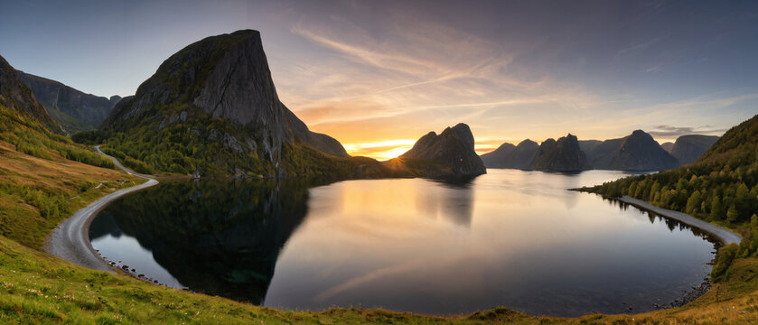 Sonnenuntergang am Fjord mit K&uuml;stenstra&szlig;e und markanten Berggipfeln