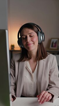 Woman listening to music with headphones while working on her laptop in a cozy office setting, vertical shot