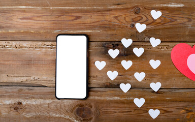 Smartphone with blank screen showing copy space by white heart shapes on wooden table