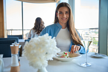 Beautiful happy young woman sitting at a restaurant eating salad