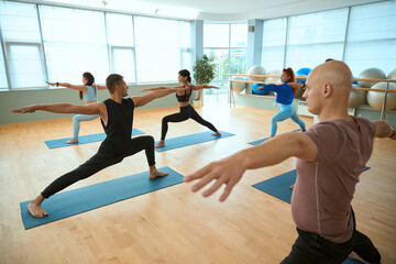 Obraz premium Group of people posing in yoga positions with their arms outstretched in group class