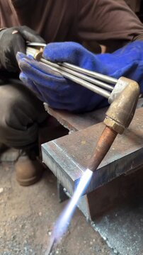 Close up of welder using oxy acetylene torch and blue protective gloves heating metal in workshop for fabrication repair and industrial training showing flame control and safety gear