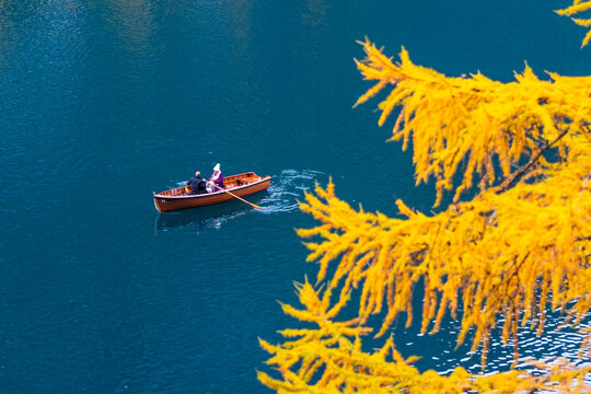 Aerial view of a rowboat with two people on a blue lake, with yellow foliage in the foreground. Braies lake,Alto Adige,Dolomites,Italy