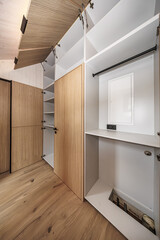 Fototapeta premium Built-in storage system featuring open wood-paneled cabinets and clean white shelves in a minimalist interior. Hardwood floors and concealed hinges. No logos visible
