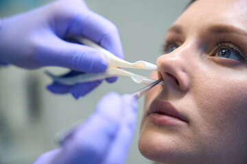 Otorhinolaryngologist checking nose with otoscope of female patient at clinic