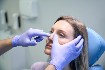 ENT doctor examines nose of female patient before rhinoplasty surgery