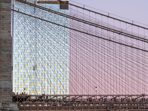 New York, United States - 04 February 2024: View of the Brooklyn Bridge's intricate cable network against a towering skyscraper, a contrast of old engineering and modern architecture.