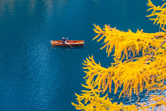 Aerial view of a person rowing a wooden boat on a blue lake, with yellow foliage in the foreground. Braies lake,Alto Adige,Dolomites,Italy