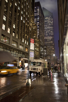 New York, United States - 28 January 2010: View of a bustling 5th Avenue bathed in the soft glow of streetlights, reflecting off the wet pavement as a yellow taxi speeds past.
