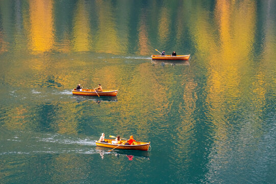 Three wooden rowboats with people on a calm lake reflecting golden trees. Braies lake,Alto Adige,Dolomites,Italy