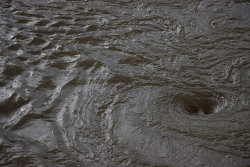Swirling whirlpool in textured surface of brown river water