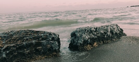 Frozen sea boulders and icy rocks on a sandy beach at sunset. Dramatic winter coast with ocean waves, salt crystals, and arctic textures. High-quality nature photography for commercial use. © Natul'ka