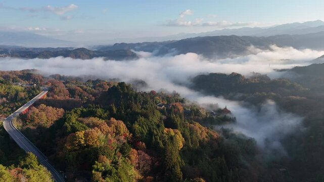 The sky is cloudy and the mountains are covered in fog. The trees are green and the leaves are changing colors