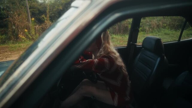 Blonde Woman In Retro Attire By Automobile. Serene Woman Resting Near Vehicle Amidst Lush Flowers