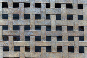 Macro view of flat woven light brown wooden splints forming rectangular grid pattern of traditional vintage snowshoe mesh with weathered organic texture against dark background.
