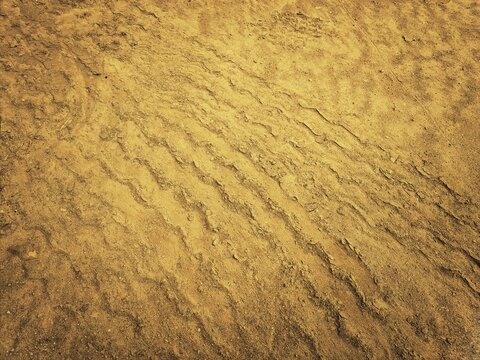
​Dry sandy soil texture with heavy machinery tire tracks and industrial earthwork patterns.