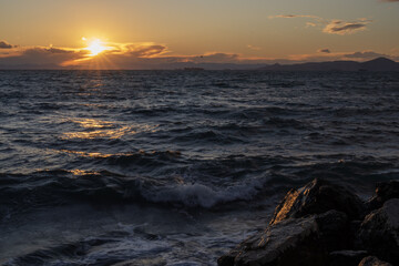 Moody sunset over the sea with textured waves and warm light reflecting on the water. Natural coastal scene conveying tranquility, power, and evening atmosphere in Athens.