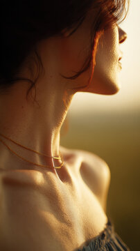 A closeup portrait of a woman's neck and collarbone glowing in warm sunlight. The gold necklace and soft light create a serene, elegant, and feminine mood.