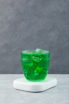 Green drink with ice cubes in glass cup, side view. Tarhun, refreshing summer drink with tarragon. Sweet non alcoholic carbonated lemonade