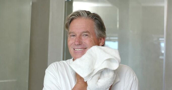 Mature man post-shower, holding white towel, dabbing face, drying hair at vanity in white tee