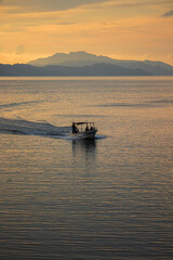 Small Tourist Boat Sailing at Sunset with Mountain Silhouette and Golden Sea Reflection