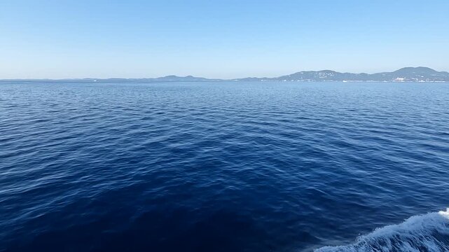 Wide shot from a moving vessel showing the white wake on deep blue Ionian Sea water with hazy mountains on the horizon, perfect for travel and nautical themes.